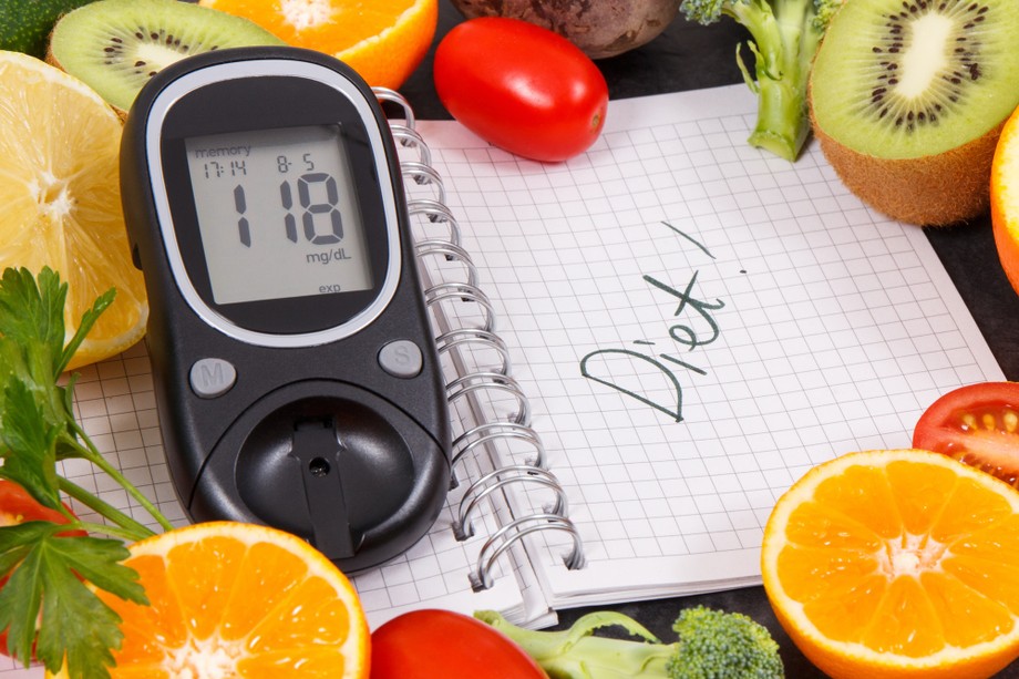 Glucometer with result of sugar level, fruits with vegetables and notepad with word diet